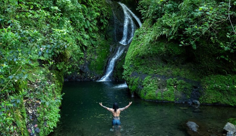 Ein Mann steht vor einem Wasserfall in Rarotonga, Cook Islands